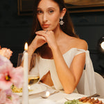 Bride wearing elegant snowflake-inspired gold plated crystal wedding earrings at a candlelit dinner, showcasing fine bridal jewelry for weddings.