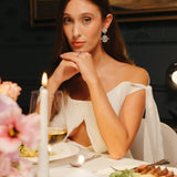 Bride wearing elegant snowflake-inspired gold plated crystal wedding earrings at a candlelit dinner, showcasing fine bridal jewelry for weddings.