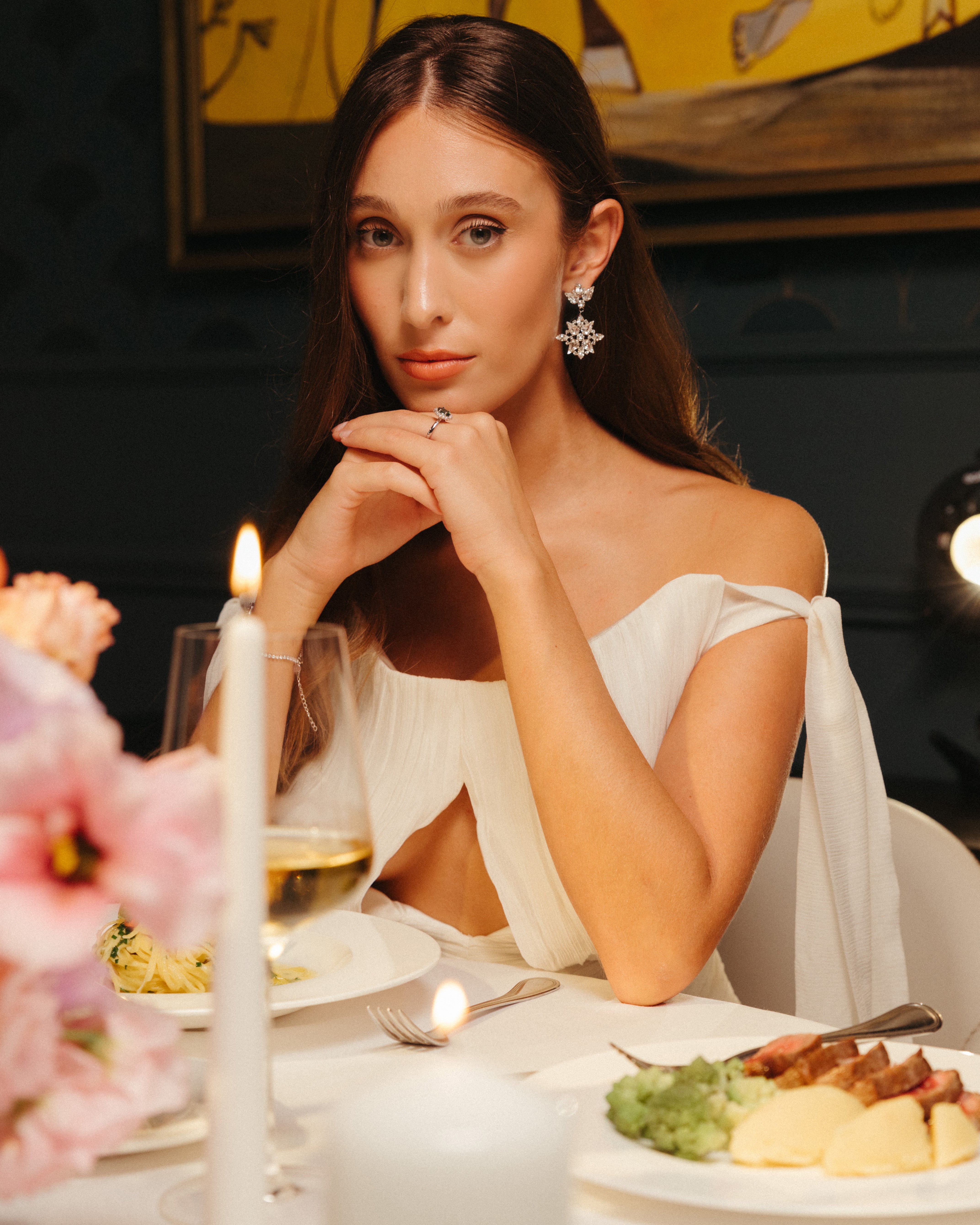 Bride wearing elegant snowflake-inspired gold plated crystal wedding earrings at a candlelit dinner, showcasing fine bridal jewelry for weddings.